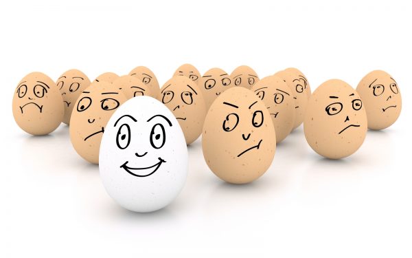 One happy smiling egg amongst sad angry and envious crowd of eggs isolated on white background